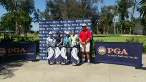 A group of five people stand with golf bags in front of a PGA Southern California Section banner on a sunny day.