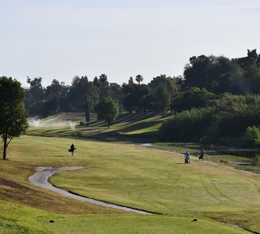 Golf course landscape with two players carrying clubs across the fairway.