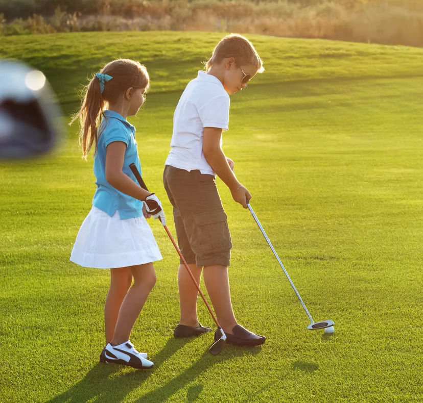 Two children playing golf on a sunlit course.