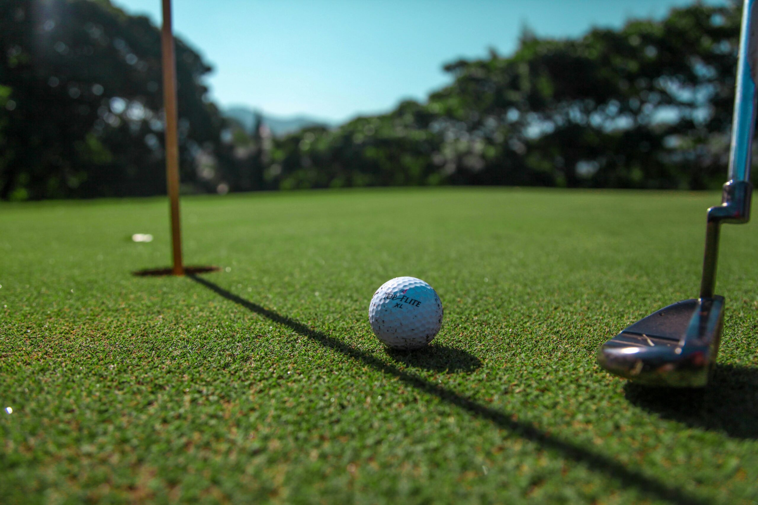 Close-up of a golf ball near a hole on a green course, with a putter poised to strike.