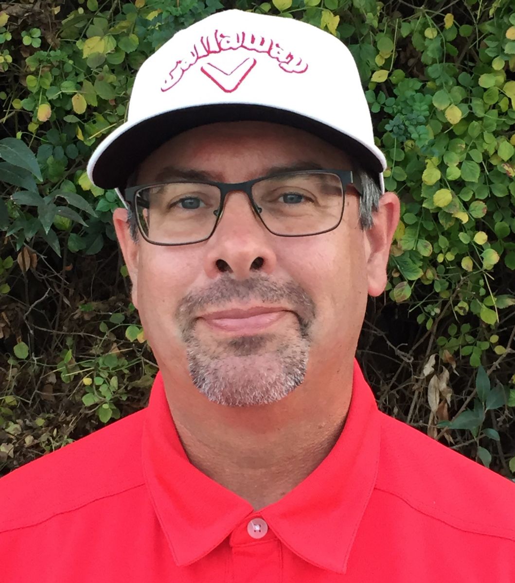 Man in glasses and a white Callaway cap, wearing a red shirt, against a backdrop of green foliage.